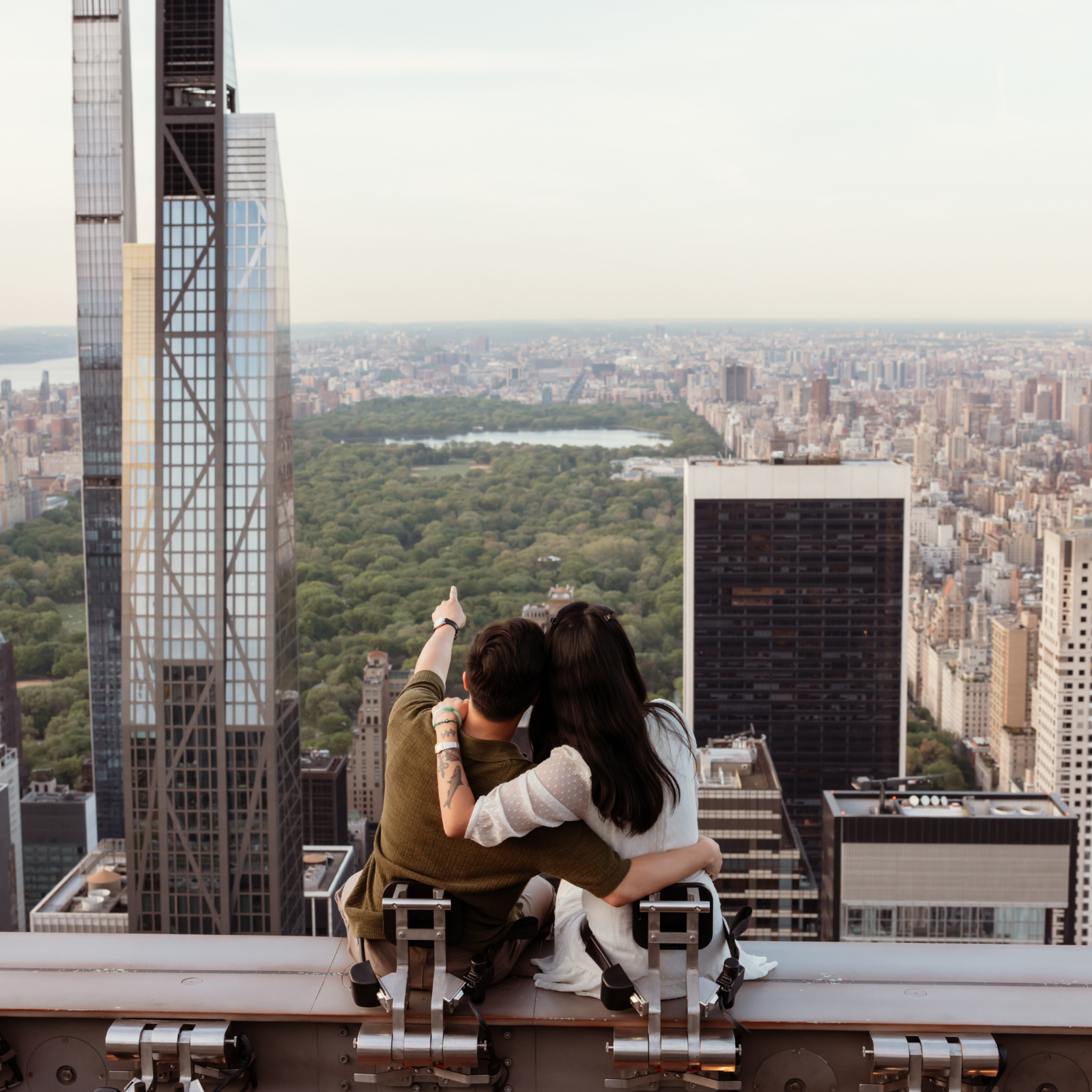 Two people enjoying the view from Top of the Rock while sitting on The Beam