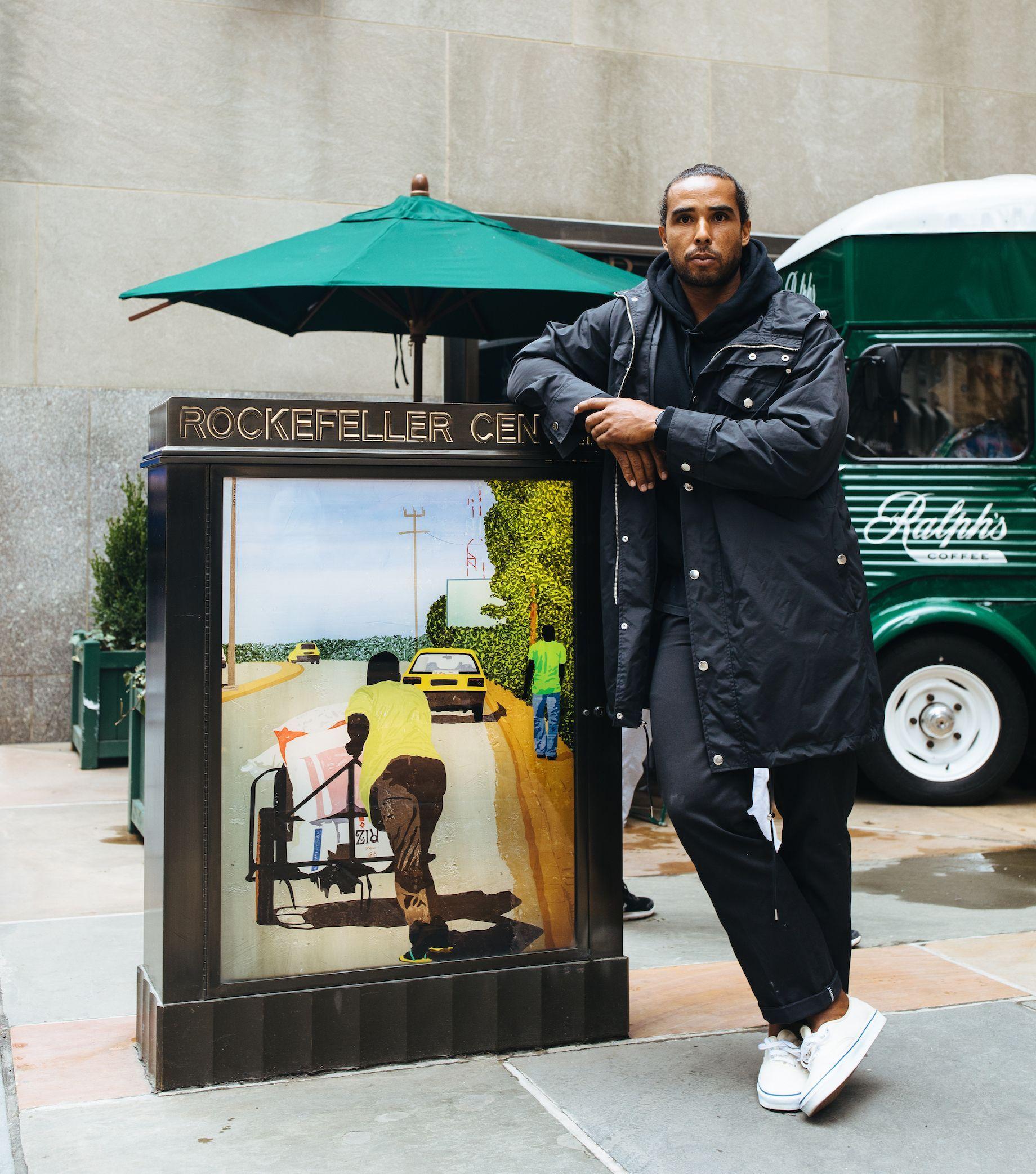 Artist Hugo McCloud stands in front of a sign featuring his work at Rockefeller Center