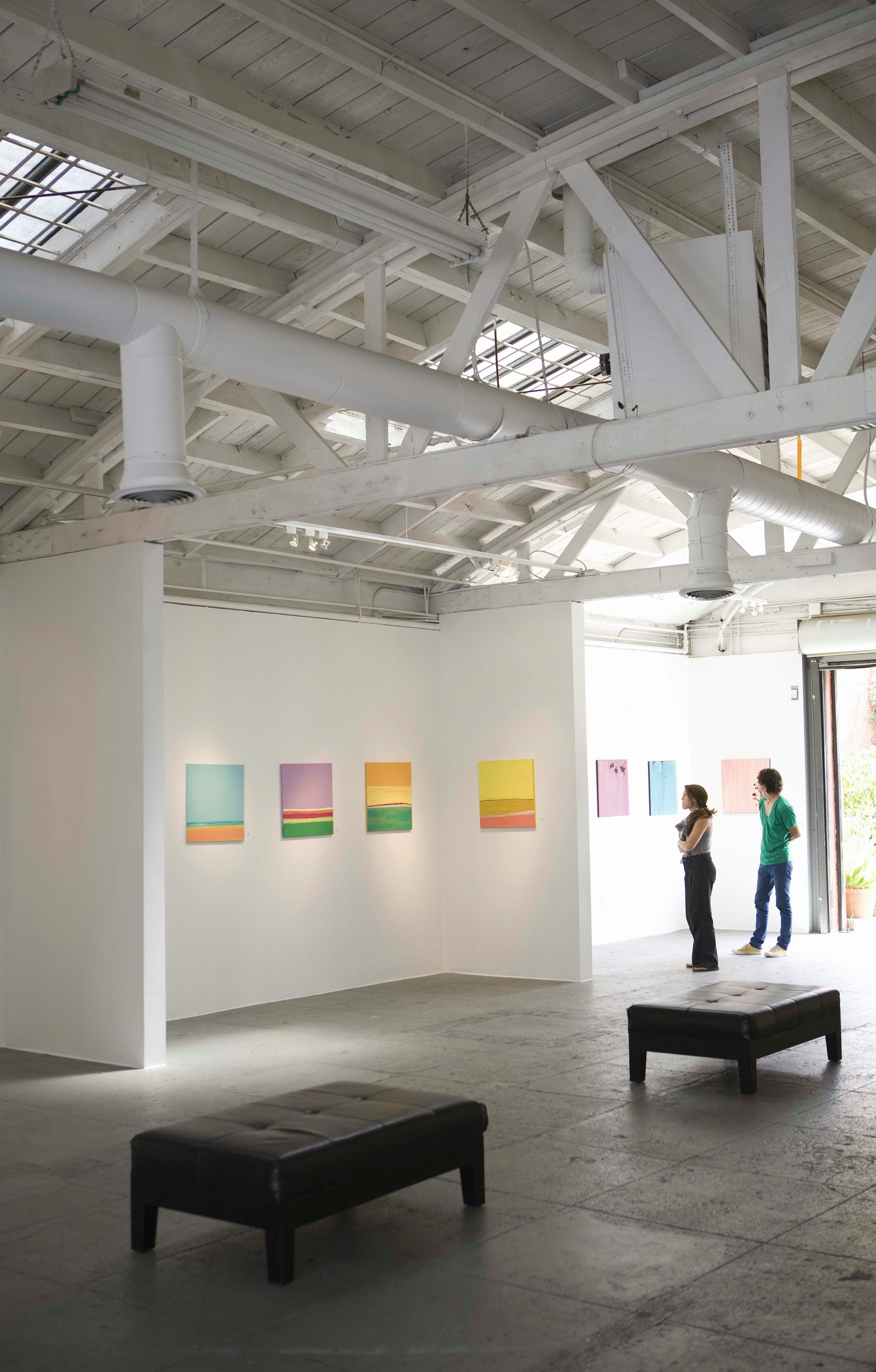 Visitors looking at paintings in a bright, open gallery space.