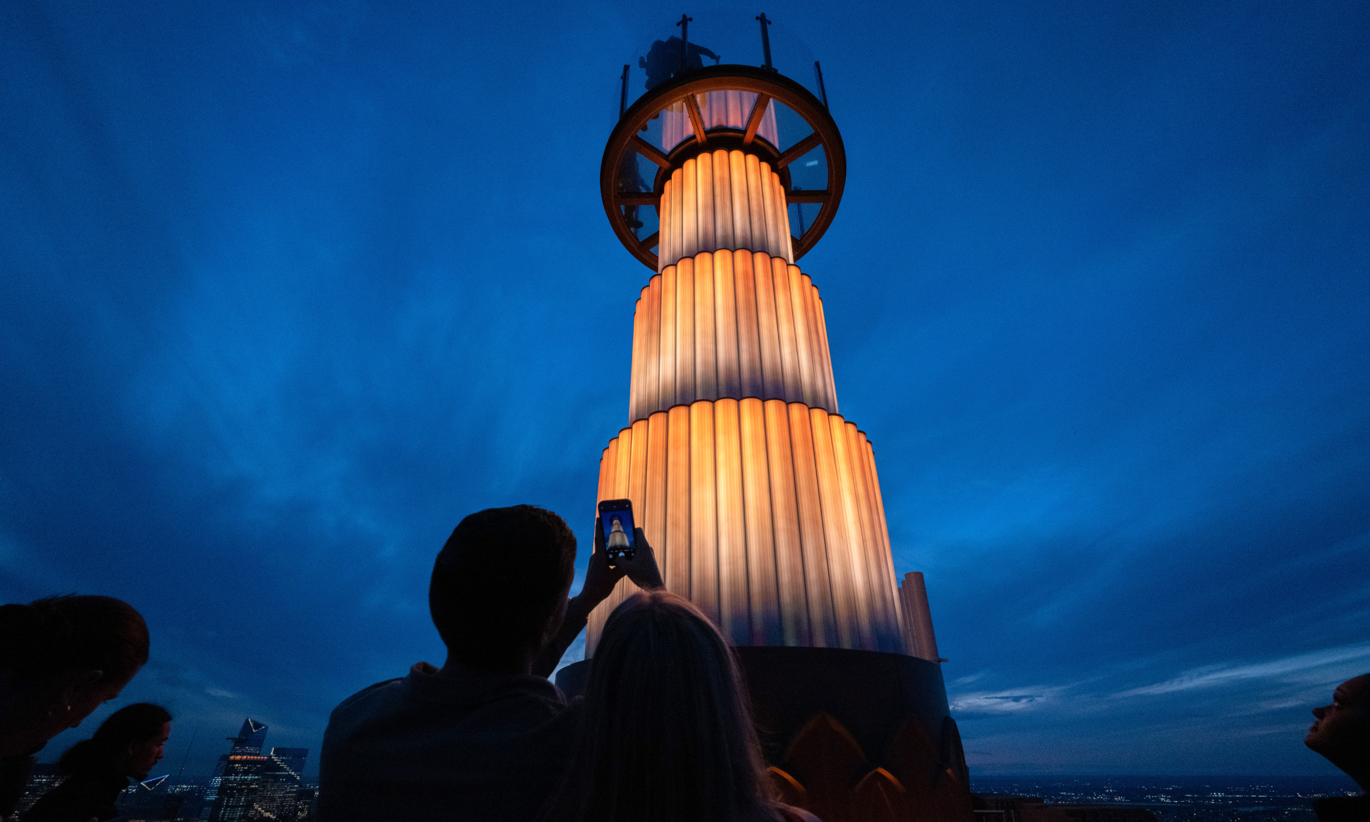 A couple taking a picture of Skylift at Top of the Rock just after sunset