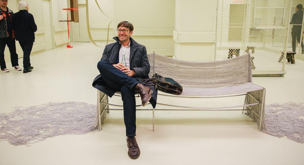 Person sitting on a chain link bench made by architect Frida Escobedo, which is featured in MASA's exhibition at Rockefeller Center