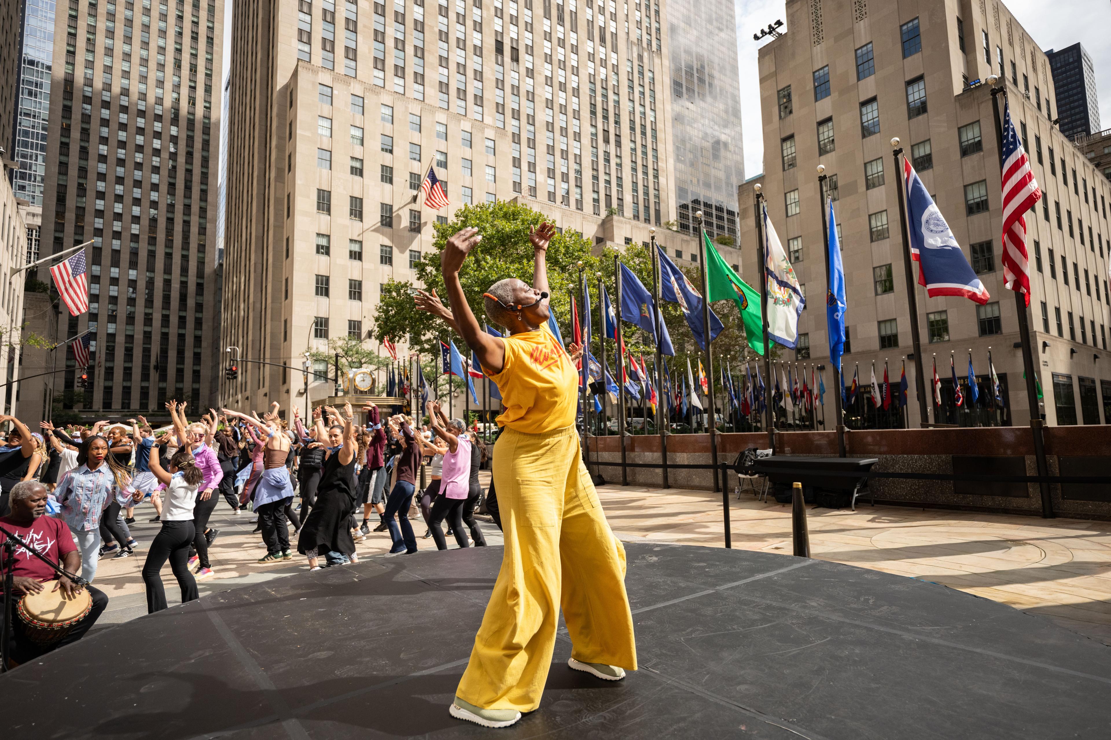 A woman in yellow leading a dance workshop at Rockefeller Center