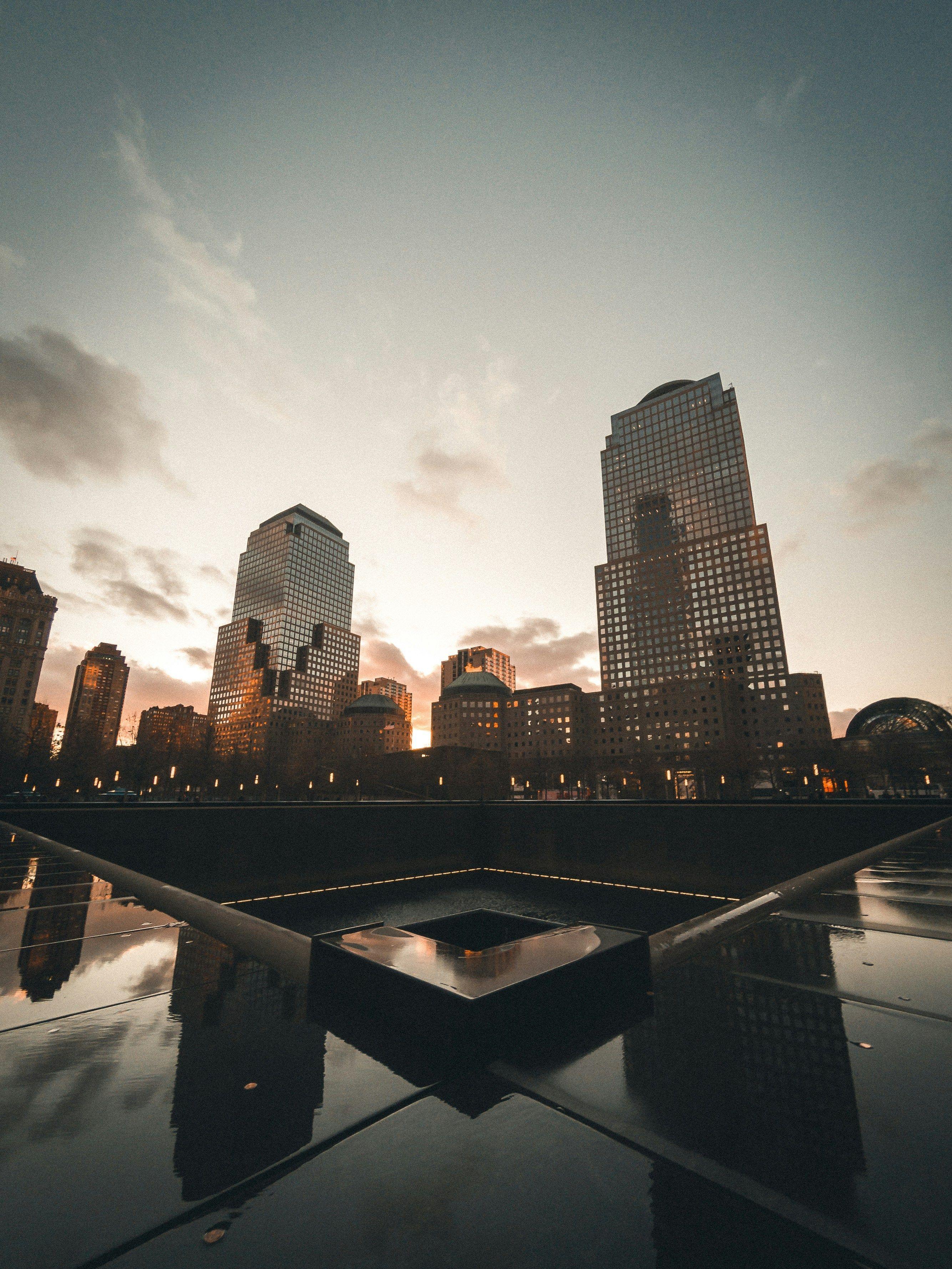 One of the 9/11 Memorial reflecting pools at sunset, with the World Trade Center site behind it.