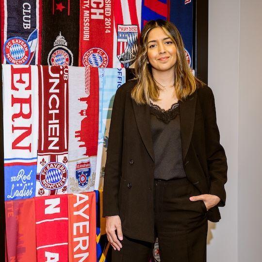 Dee Kundra standing in front of a collage of FC Bayern scarves