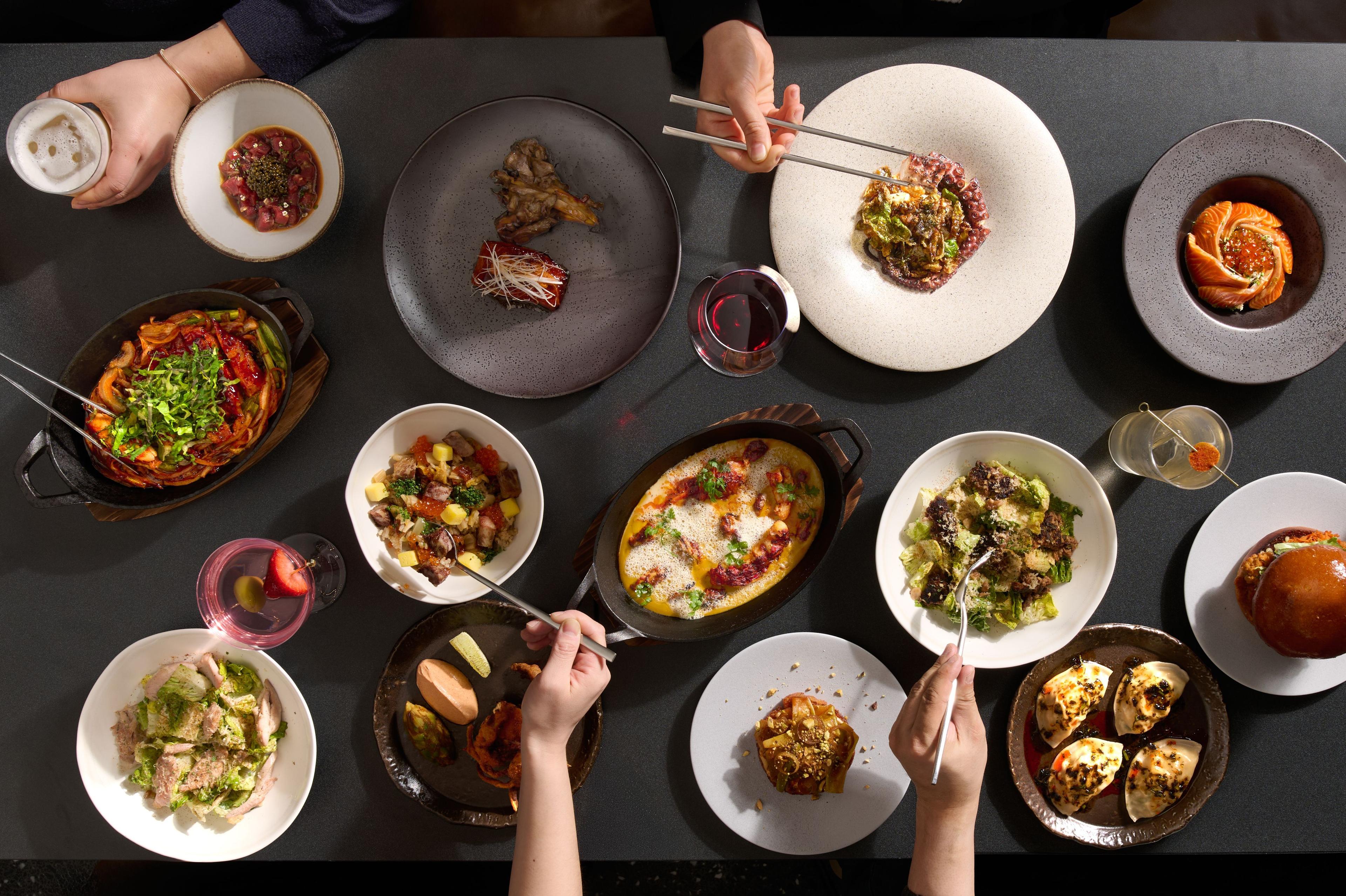 A table with various dishes with hands holding chopsticks at Naro
