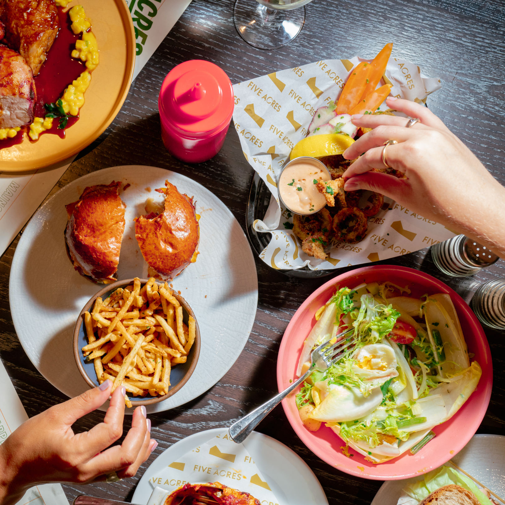 Two hands reaching for plates of food at 5 Acres at Rockefeller Center