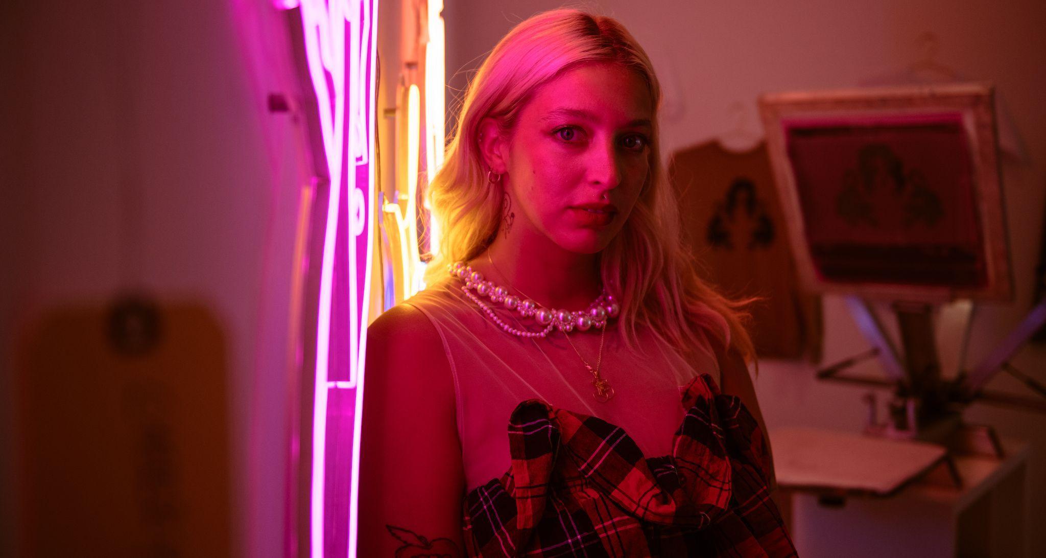 Artist Mira Mariah poses in front of neon sign