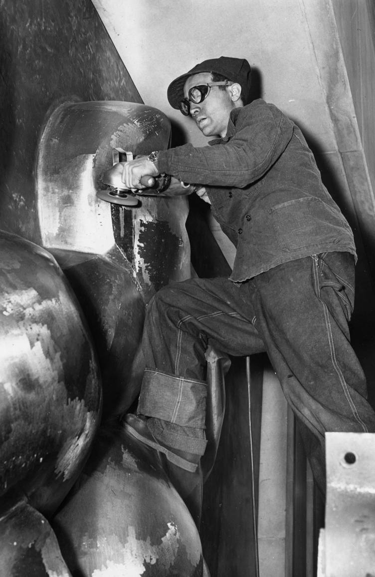 Black and white photo of artist wearing goggles sculpting metal works